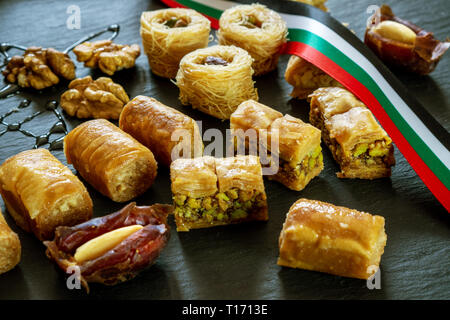 Tipo diverso di arabian baklava e le date su sfondo nero con spazio per i tipi di testo - nido borma ush-el-bul-bul asabi con UAE RIBBON COLORE Foto Stock