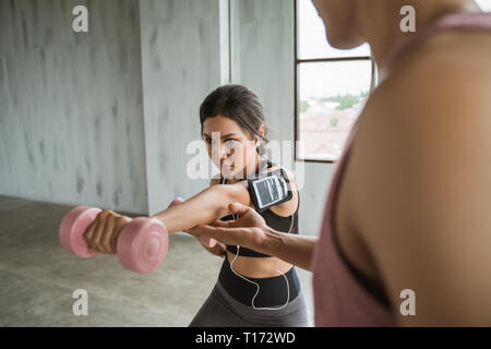 Asian giovane donna facendo esercizi di peso con l'assistenza del suo personal trainer Foto Stock