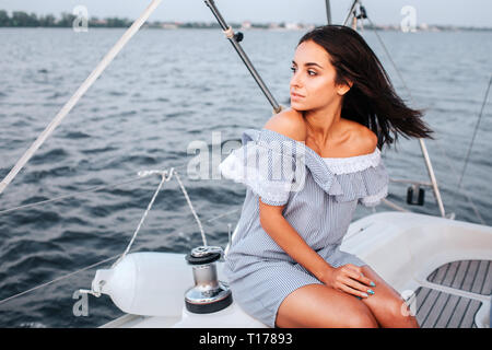 Incredibile e bella giovane donna seduta a bordo di yacht e guardare a sinistra. Lei è calma e tranquilla. La donna è da solo. Foto Stock