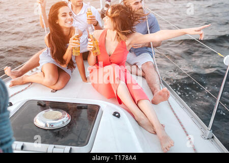 Vista di taglio del ypung le donne sedute davanti agli uomini. Signora in abito rosso punto a destra. Bruna la guarda e sorrisi. Sono felice. Gli uomini sono alla ricerca Foto Stock