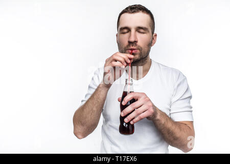 Un ragazzo con taglio corto è di bere il coke dalla bottiglia attraverso la paglia. Questo uomo piace mangiare fast food e bere bevande dolci. Isolato su bianco Foto Stock