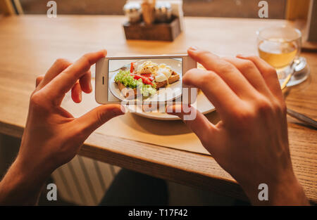 Mani dell'uomo è in possesso di telefono cellulare e di scattare una foto di gustoso pasto sulla piastra. È colorata e deliziosa Foto Stock