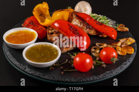 Rosso arrosto peperoni servita con carne di maiale alla griglia medaglioni, pomodoro, aglio e ciotole di salsa di immersione Foto Stock