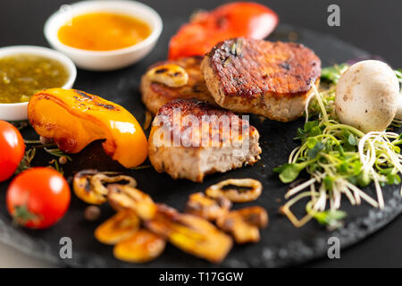 Arrosto di filetto di maiale con peperoni e aglio servito con insalata germogli di soia, funghi e ciotole di salsa appetitosa Foto Stock