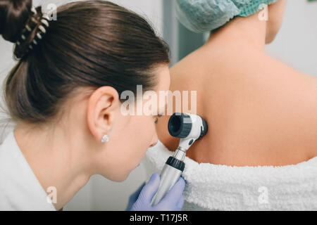 Il dermatologo esamina birthmarks sulla pelle del paziente con un dermatoscope Foto Stock