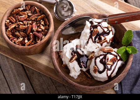 Vista aerea del gelato alla vaniglia e rabboccato con lo sciroppo al cioccolato e le noci pecan in una ciotola di legno Foto Stock