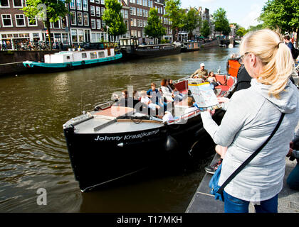 Donna adulta in piedi sulla riva del canale guardando il volantino informativo sulle gite in barca da diporto attraverso i canali di Amsterdam, Olanda, Europa. Foto Stock