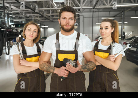 Bella donna e uomo bello indossare in marrone tute, white t shirt lavorando come meccanica. Brutale uomo muscoloso e belle ragazze azienda strumenti, guardando la telecamera, in posa. Foto Stock