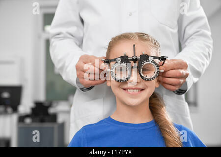 Oculista in camice bianco utilizzando speciali attrezzature mediche per la salute degli occhi, Controllo vista. Sorridente ragazza seduta e guardando la telecamera attraverso test di bicchieri. Foto Stock