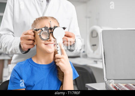 Professional oculista in bianco cappotto medico controllare gli occhi della ragazza adolescente con equipaggiamento speciale in clinica medica. Bella ragazza che indossa gli occhiali di prova, seduta e sorridente. Foto Stock