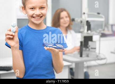 Pretty girl holding vetri azzurrati e contenitore con lenti. Medico oculista in clinica aiuta a scegliere il meglio per la salute della vista. Le lenti a contatto alternativa ai bicchieri. Foto Stock