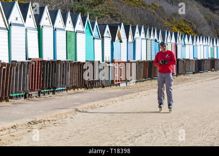 Bournemouth Dorset, Regno Unito. 24 mar 2019. Regno Unito: meteo bella giornata di sole con un cielo azzurro e il sole caldo a Bournemouth spiagge, come i visitatori in testa al mare per rendere la maggior parte del tempo splendido. L'uomo il pattinaggio su pattini a rotelle in linea lungo la promenade passato capanne sulla spiaggia. Credito: Carolyn Jenkins/Alamy Live News Foto Stock