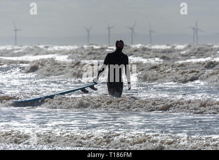 Formby, Merseyside, Regno Unito. 24 mar 2019. Guardando come uno di Anthony Gormley' s figure è venuto a vita, un ardito surfer sulla spiaggia a Formby, Merseyside, su un brillante ma freddo e blustery giorno. Credito: John Eveson/Alamy Live News Foto Stock