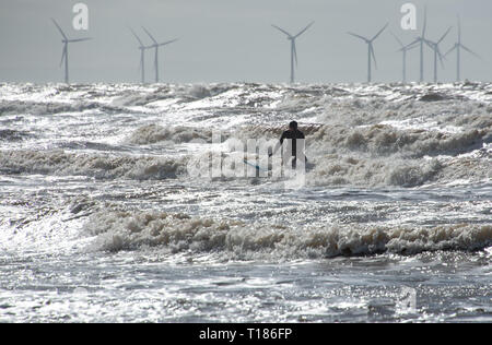 Formby, Merseyside, Regno Unito. 24 mar 2019. Guardando come uno di Anthony Gormley' s figure è venuto a vita, un ardito surfer sulla spiaggia a Formby, Merseyside, su un brillante ma freddo e blustery giorno. Credito: John Eveson/Alamy Live News Foto Stock