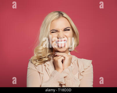 Funny cute giovane donna sorridente, winking e che mostra la linguetta su sfondo rosa. Donna con la lingua fuori ritratto Foto Stock