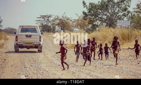 Gruppo di himba i bambini a correre verso il off-road vetture di turisti vicino al Epupa Falls in Namibia Foto Stock