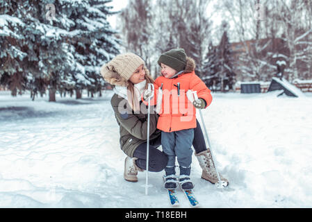 Un felice madre aiuta il suo bambino, ragazzo di 3-6 anni, stand i bambini gli sci, la gioia di un sorriso è divertente. Primi passi nella pratica dello sci. Supporto di apprendimento, Foto Stock