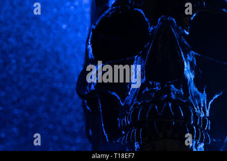 Umano cranio blu su sfondo scuro con bokeh di fondo. Concetto di paura, di morte e di orrore, festa di Halloween. Spooky e funesta. Foto Stock