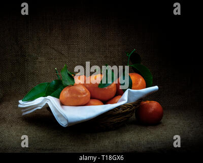 Arance con foglie nel cestello, scuro in stile ciaroscuro ancora in vita. La frutta in Assia . Foto Stock