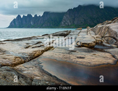 La spiaggia sassosa con bagni di marea a Ersfjord, Senja, Norvegia. Estate giorno polare notte costa. I denti di drago di roccia nel lontano. Foto Stock