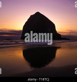 Silhouette con la riflessione di Haystack Rock, monumento naturale della costa del Pacifico, al tramonto. Scenario paesaggistico di Oregon, Cannon Beach, Stati Uniti d'America. Foto Stock