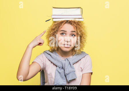 Ragazza è ponting sul libro che sono sulla sua testa. Ella è frustrato. La ragazza non sa cosa fare con loro Foto Stock