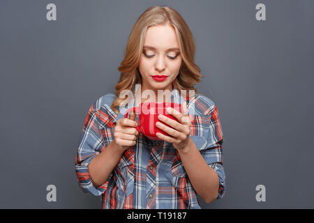 Ragazza seria azienda è grande e rosso coppa e lo sta guardando. Ella è molto concentrata. Isolato su sfondo grigio Foto Stock