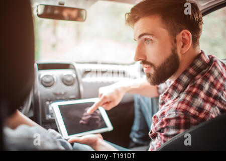 Bello e barbuto ragazzo è in possesso di un bianco tablet e rivolta verso lo schermo. Egli sta cercando per il suo partner e a parlare con lui Foto Stock