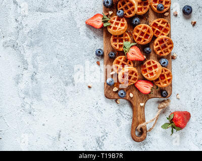 Piccolo giro soft deliziosi waffles belgi sul bordo di taglio. Fresca cialde belghe con frutti di bosco e salsa di caramello vista dall'alto. Copia spazio per testo o mock up Foto Stock