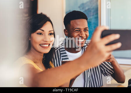 Donna prendendo selfie con il suo amico al cafe. Riunione amici presso il cafe tenendo autoritratto con smart phone per creare contenuti per i social media. Foto Stock