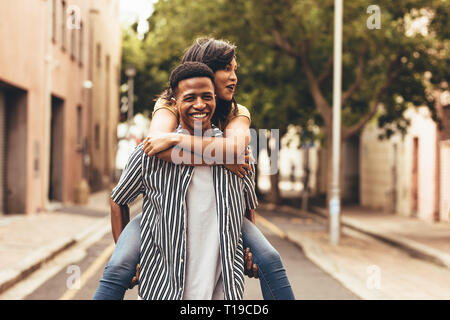 Uomo che porta una donna sulla sua schiena. Giovane piggybacking all'aperto sulla strada della citta'. Foto Stock