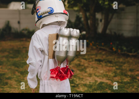 Vista posteriore del ragazzo nello spazio casco e tuta portando un giocattolo jetpack sul suo retro. Ragazzo che finge di essere un astronauta giocando all'esterno. Foto Stock