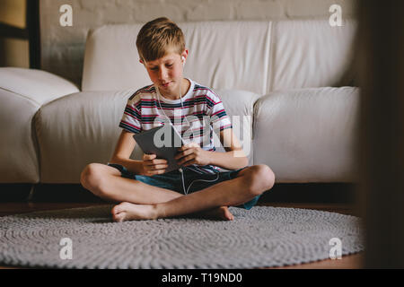 Ragazzo seduto sul pavimento che indossa gli auricolari e giocare con i videogiochi su tavoletta digitale. Ragazzo in cuffie giocando online gioco su tablet a casa.