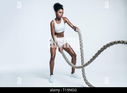donna fitness che usa le corde per l'allenamento per gli esercizi. Atleta che si allena con corde da battaglia su sfondo bianco. Foto Stock