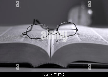 Vista ravvicinata di occhiali da lettura su un libro in bianco e nero Foto Stock