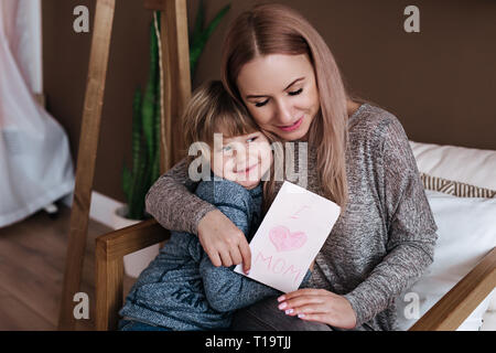 Felice Festa della mamma. Bambino figlio si congratula con MOM e dà la sua cartolina. Madre e figlio miling e avvolgente. Foto Stock