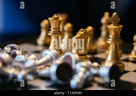 Closeup colpo di golden scacchi pezzi posti vicino al mucchio di argento persi sulla scacchiera Foto Stock