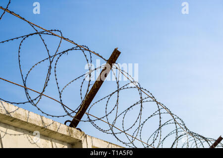 Parete in cemento con rasoio nastro spinato filo sul cielo blu sullo sfondo Foto Stock