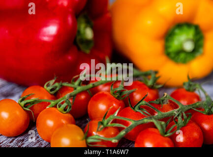 Un giallo e rosso peperoncino (capsicum) e i pomodori ciliegia sulla vite. Foto Stock