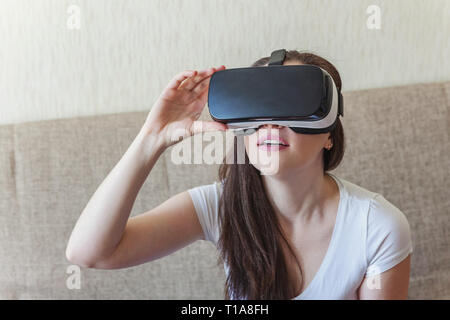 Smile giovane donna indossa utilizzando la realtà virtuale VR occhiali casco auricolare sul divano di casa. Lo smartphone utilizzando con la realtà virtuale gli occhiali. Tecnologia, Foto Stock