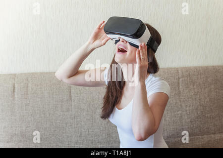 Smile giovane donna indossa utilizzando la realtà virtuale VR occhiali casco auricolare sul divano di casa. Lo smartphone utilizzando con la realtà virtuale gli occhiali. Tecnologia, Foto Stock