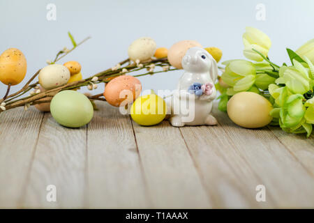 Primavera Pasqua sfondo su tavola di legno con bianco di coniglio in ceramica colorata e tulipani e uova spazio per testo Foto Stock