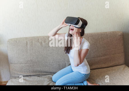 Smile giovane donna indossa utilizzando la realtà virtuale VR occhiali casco auricolare sul divano di casa. Lo smartphone utilizzando con la realtà virtuale gli occhiali. Tecnologia, Foto Stock