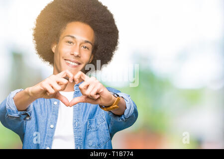 Giovane americano africano uomo con capelli afro sorridente in amore che mostra il simbolo del cuore e la forma con le mani. Concetto romantico. Foto Stock