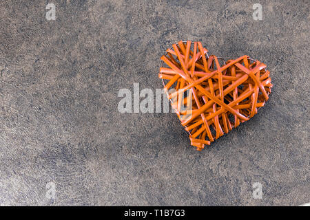 Arancione a forma di cuore la tessitura di paglia su un grigio Sfondo testurizzata Foto Stock