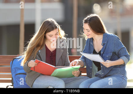 Due felici gli studenti di confronto note seduta su una panchina nel parco Foto Stock