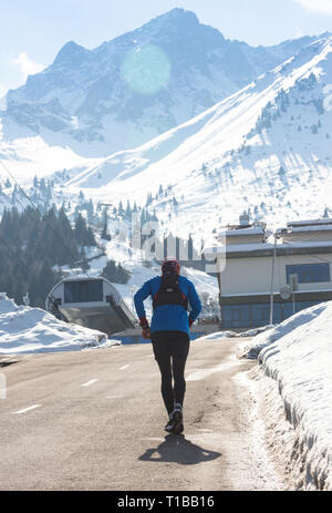 Giovani sport sano uomo in esecuzione su strada asfaltata a neve montagne in runner duro allenamento in energia e endurance concetto con un bel freddo Foto Stock