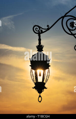 Vicino la vista laterale della vecchia vintage antica strada lampada lanterna brillante sole serale e brillanti Cielo di tramonto Foto Stock