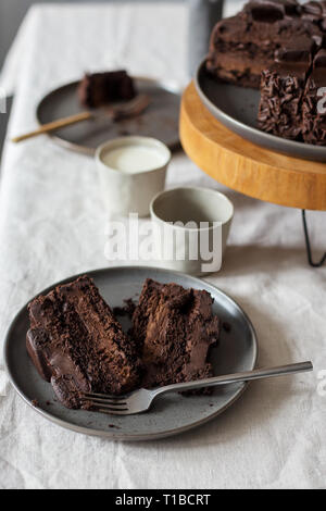 Pezzi di torta al cioccolato su lastra grigia, tutta la torta sul supporto in legno e vetro con latte sul tavolo. Concetto di dessert set tavola Foto Stock