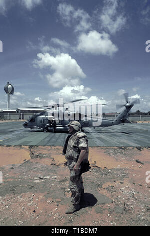 Il 29 ottobre 1993 A U.S. Soldato dell'esercito si erge in primo piano come un US Navy Sikorsky SH-60 Seahawk elicottero dall'USS Abraham Lincoln si prepara per il decollo dalla heli-pad a UNOSOM HQ a Mogadiscio, in Somalia. Foto Stock